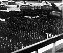 КТ Заксенхаузен – перекличка на табірному майдані, удалині на бараках текст імовірно такого змісту: „Es gibt nur einen Weg zur Freiheit, seine Meilensteine heissen: Gehorsam – Fleiss – Ehrlichkeit – Ordnung – Sauberkeit –Nüchternheit – Wahrhaftigkeit – Opfersinn und Liebe zum Vaterland” (Є тільки один шлях до свободи, його наріжні камені називаються: послух – ретельність – чесність – порядок – чистота – тверезість – щирість – жертовність і любов до батьківщини); 1939 р. (IPN)